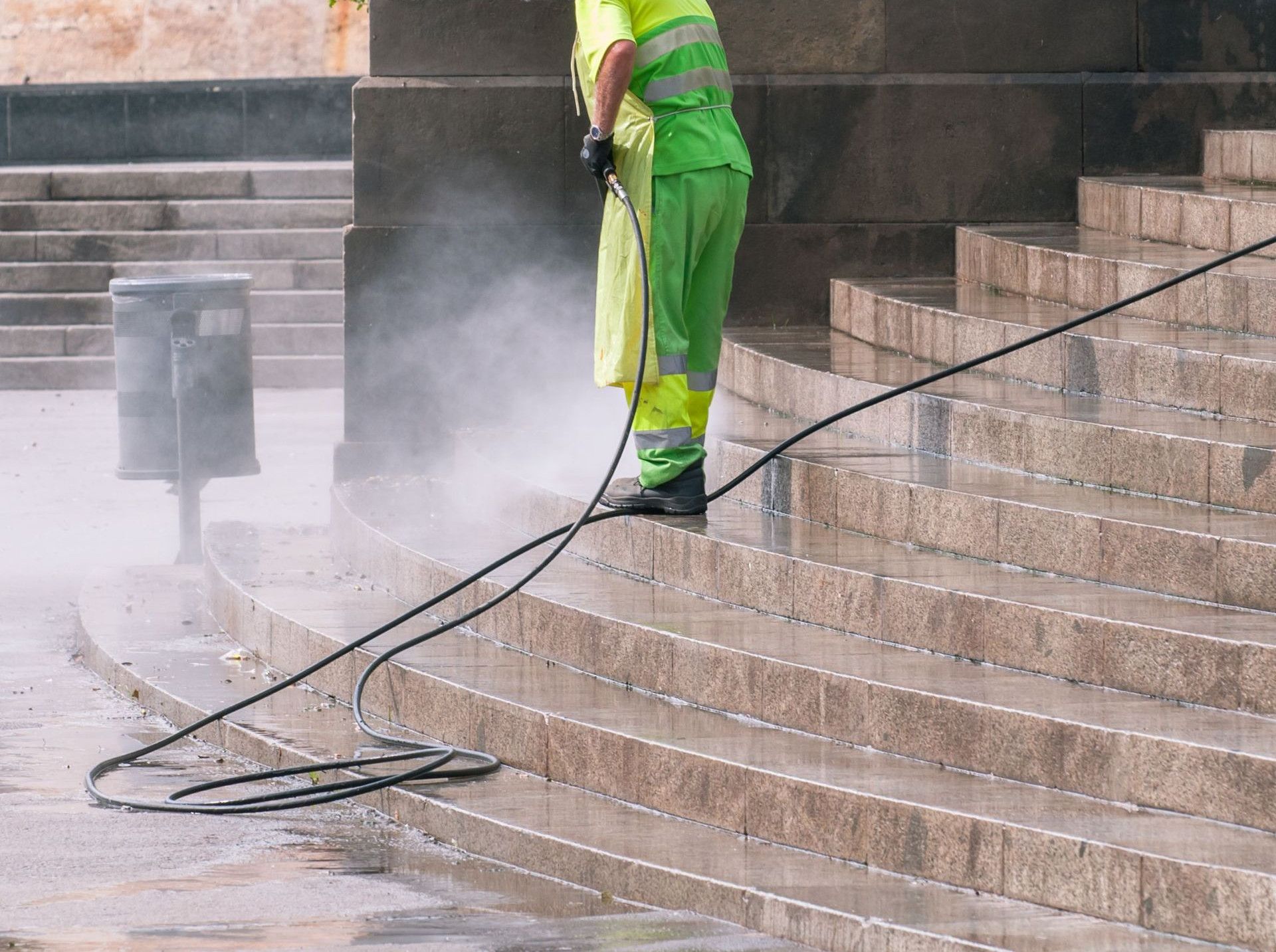 A street worker pressure washes stone stairs in a public park, ensuring cleanliness and safety.