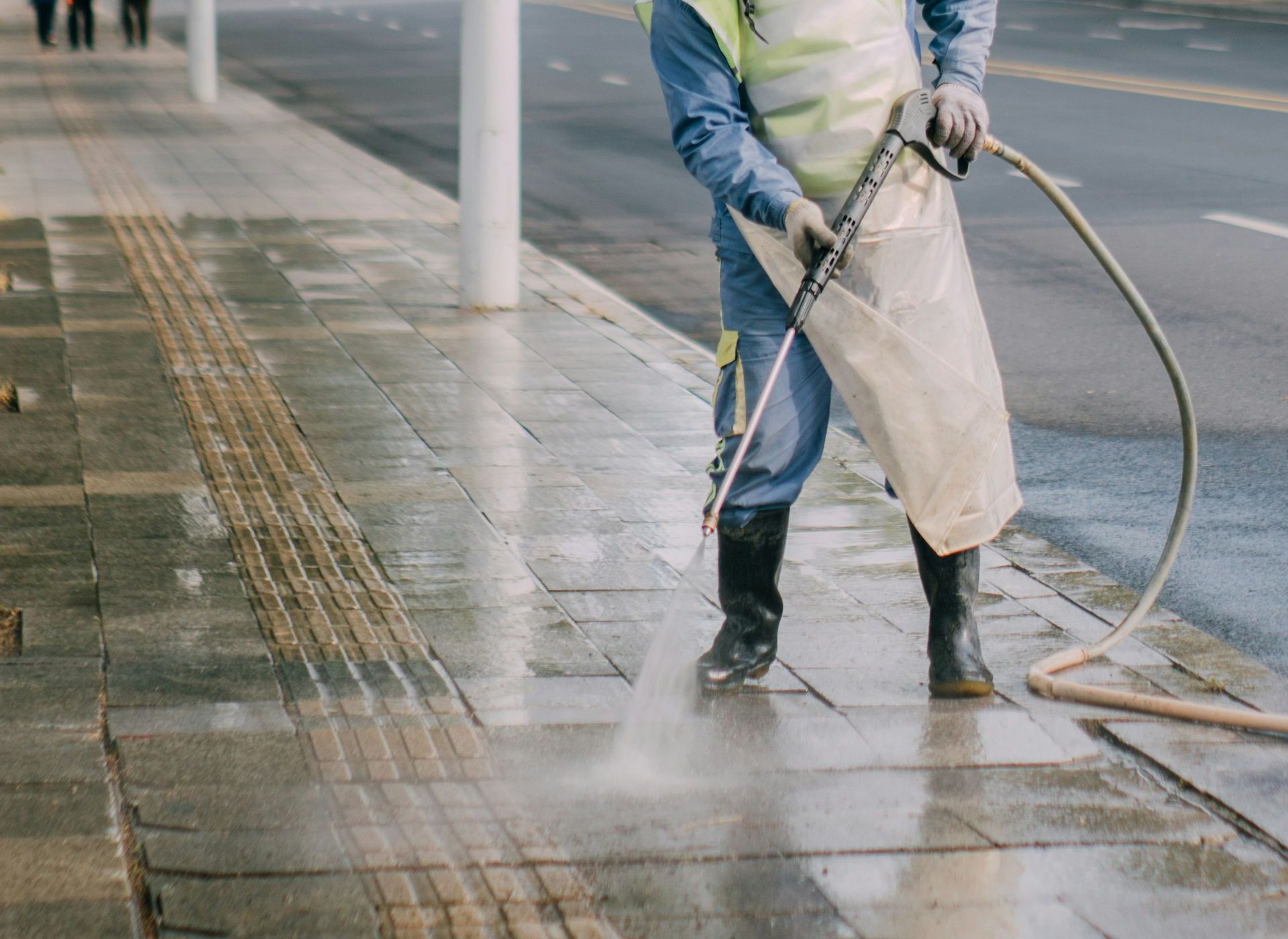 a man in a yellow vest is spraying water on a sidewalk